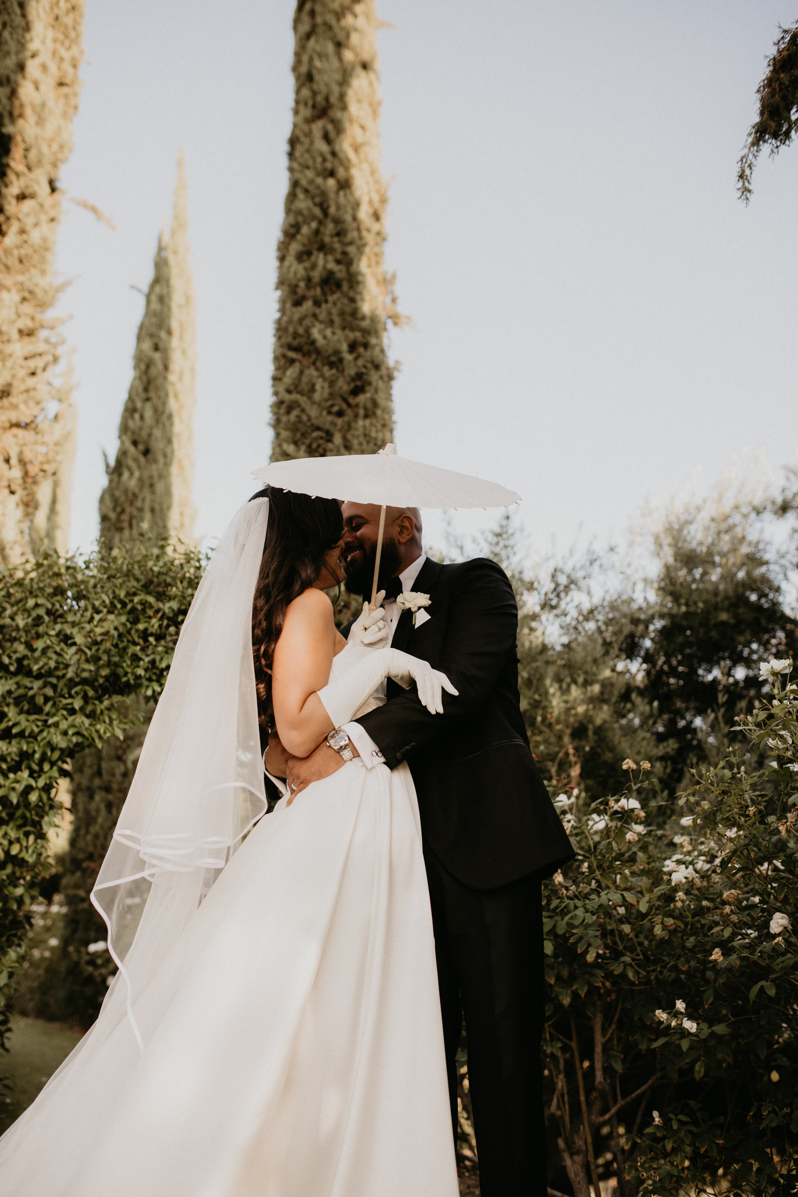 Bride and groom embracing under a white parasol in a garden