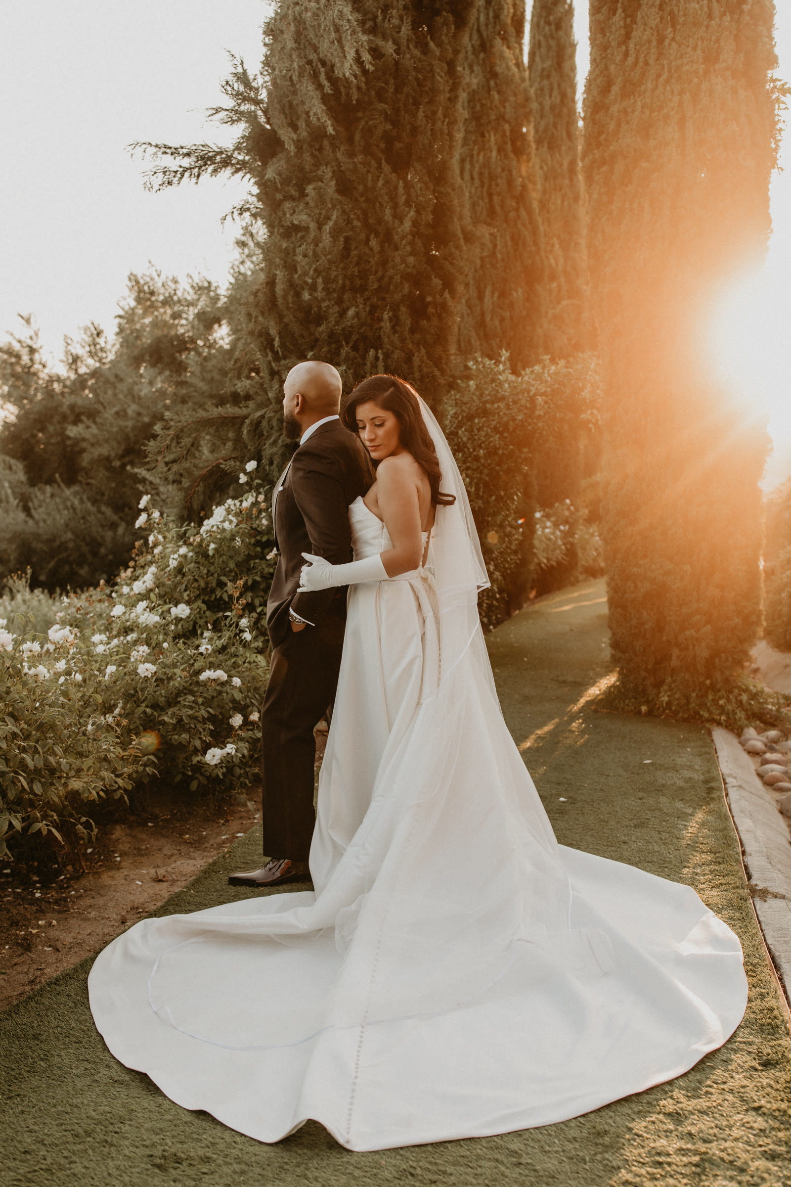 Bride in a white gown and gloves with groom on a lawn at sunset